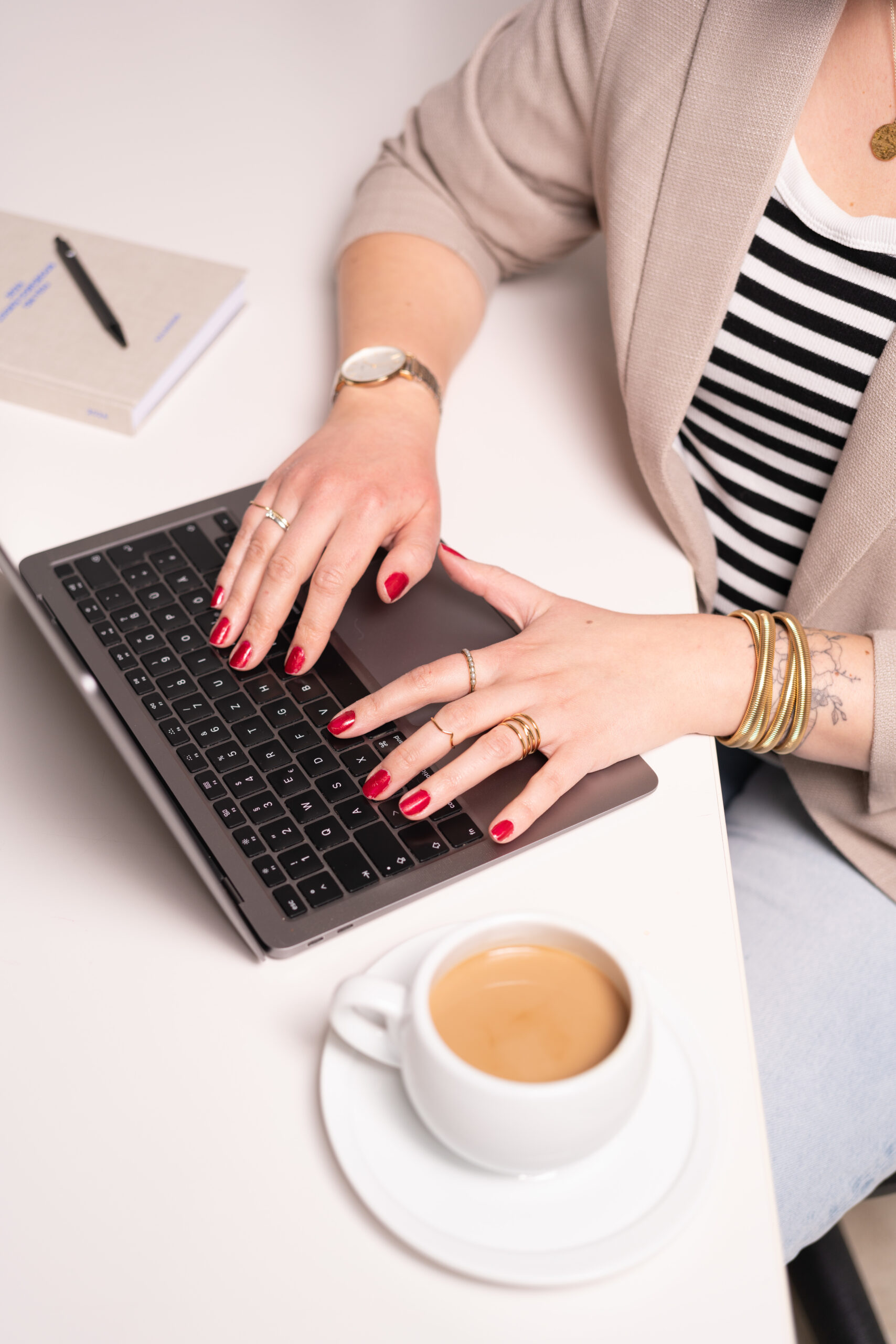 Nadine von Content Instinct am Laptop. Man sieht nur ihre Hände. Neben dem Laptop steht ein Milchkaffee.