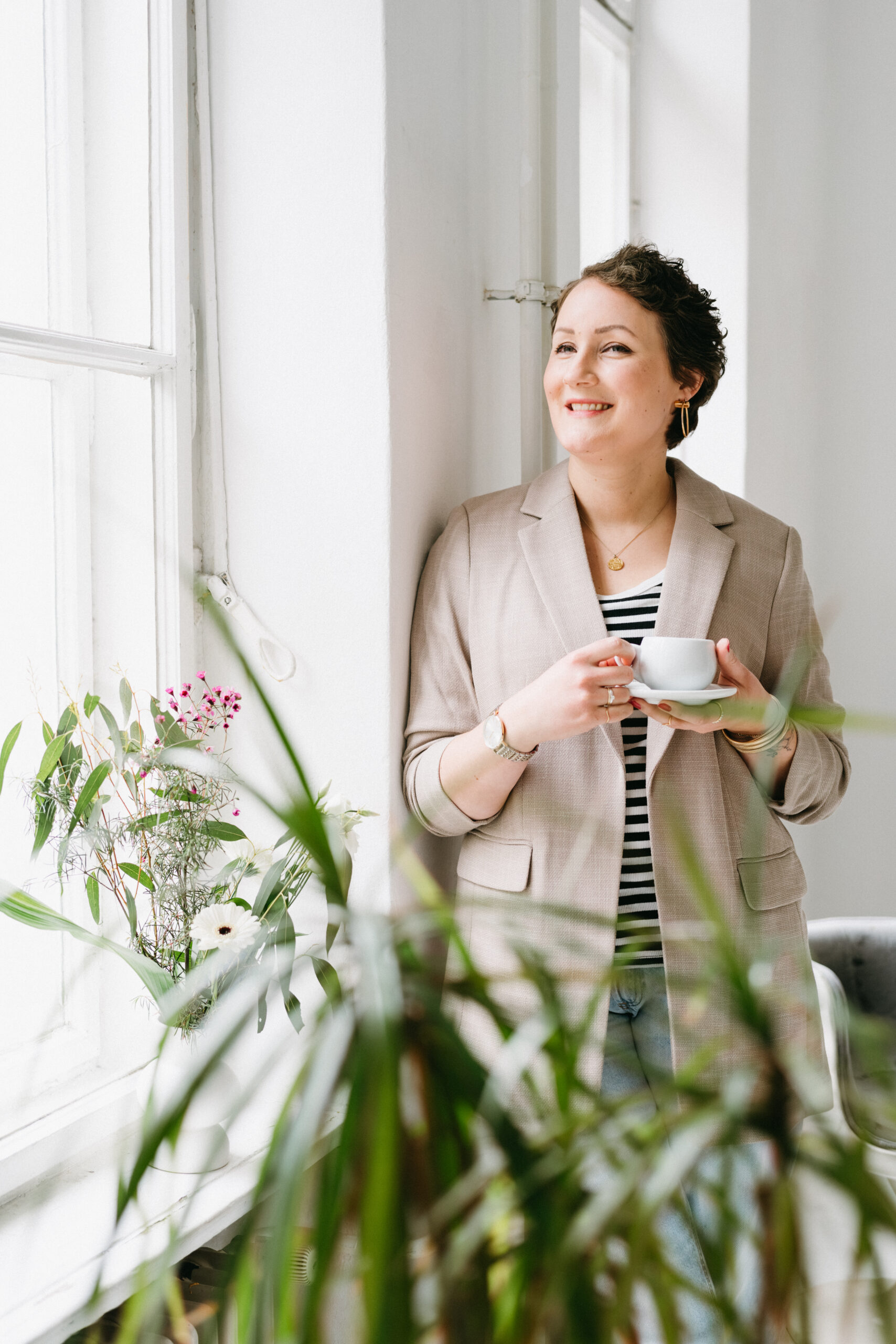 Nadine von Content Instinct steht lächelnd mit einem Kaffee am Fenster.