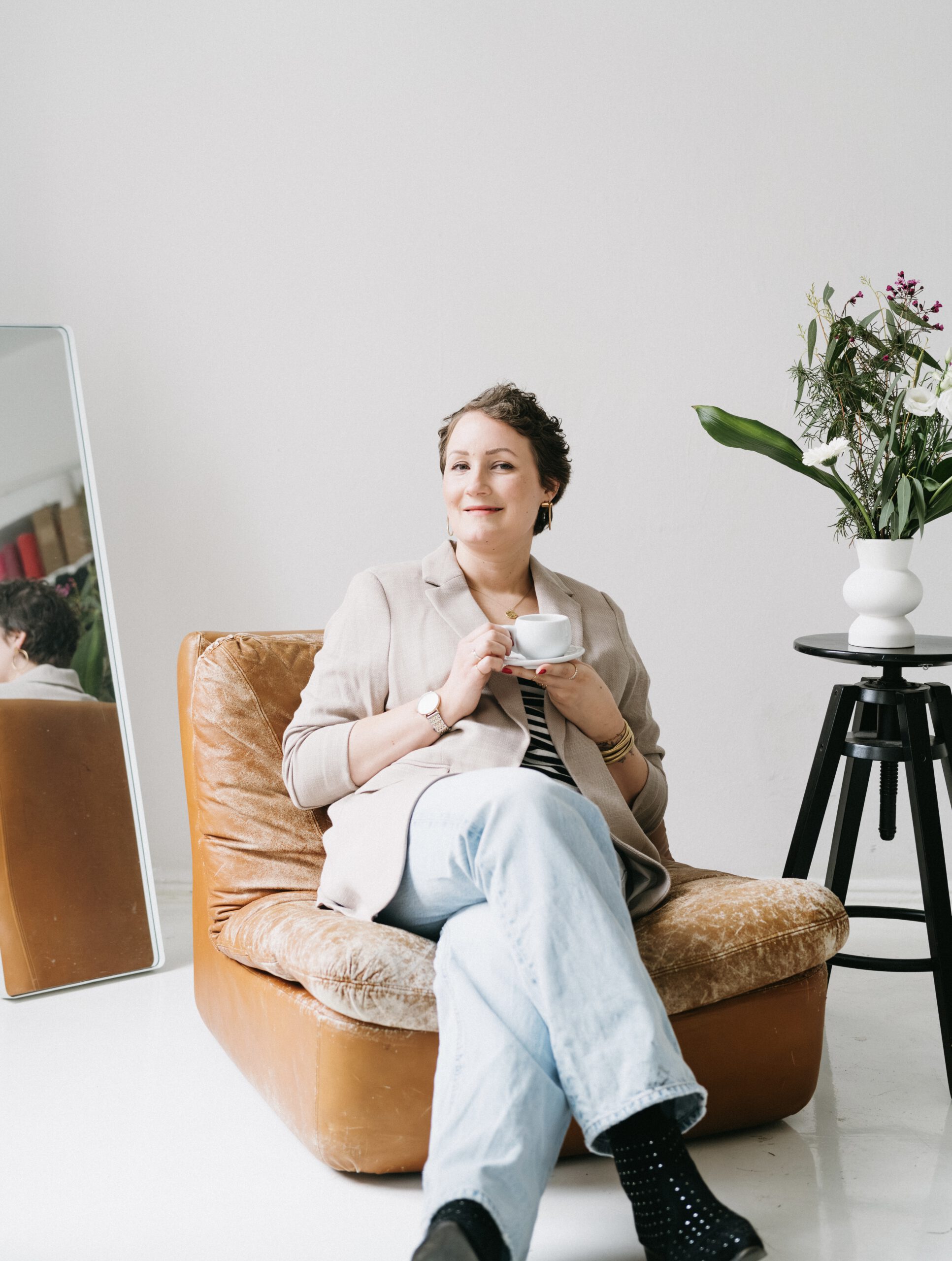 Nadine von Content Instinct sitzt lächelnd auf einem Vintage-Sessel und trinkt einen Kaffee.